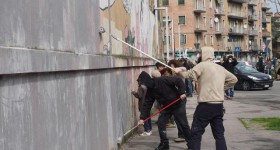 Lo street artist Blu, che già ha cancellato suoi murales a Berlino, raduna una piccola folla a Bologna davanti al suo dipinto più conosciuto, la 'battaglia' che adorna il centro sociale Xm24, mentre una 'squadra' di imbianchini lavora accompagnata dalla musica della Banda Roncati, Bologna, 12 marzo 2016. ANSA/ GIORGIO BENVENUTI