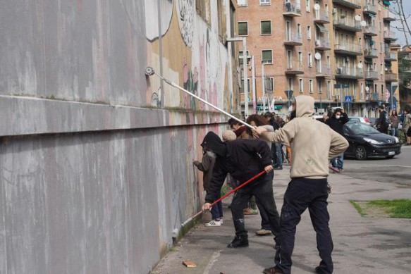 Lo street artist Blu, che già ha cancellato suoi murales a Berlino, raduna una piccola folla a Bologna davanti al suo dipinto più conosciuto, la 'battaglia' che adorna il centro sociale Xm24, mentre una 'squadra' di imbianchini lavora accompagnata dalla musica della Banda Roncati, Bologna, 12 marzo 2016. ANSA/ GIORGIO BENVENUTI